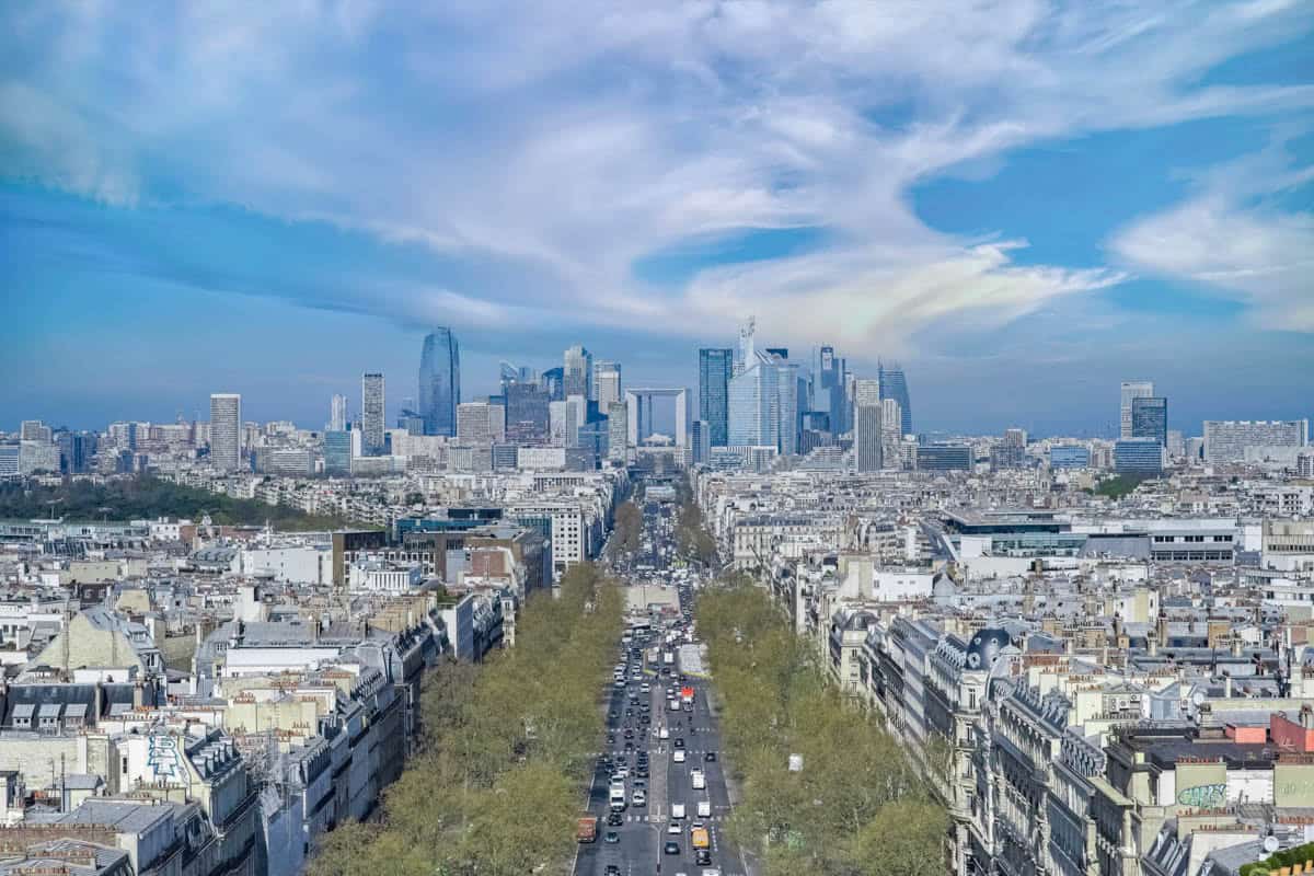 Arc de Triomphe in Paris, France pairs avenue extending toward the modern La Défense skyline with cityscape details.