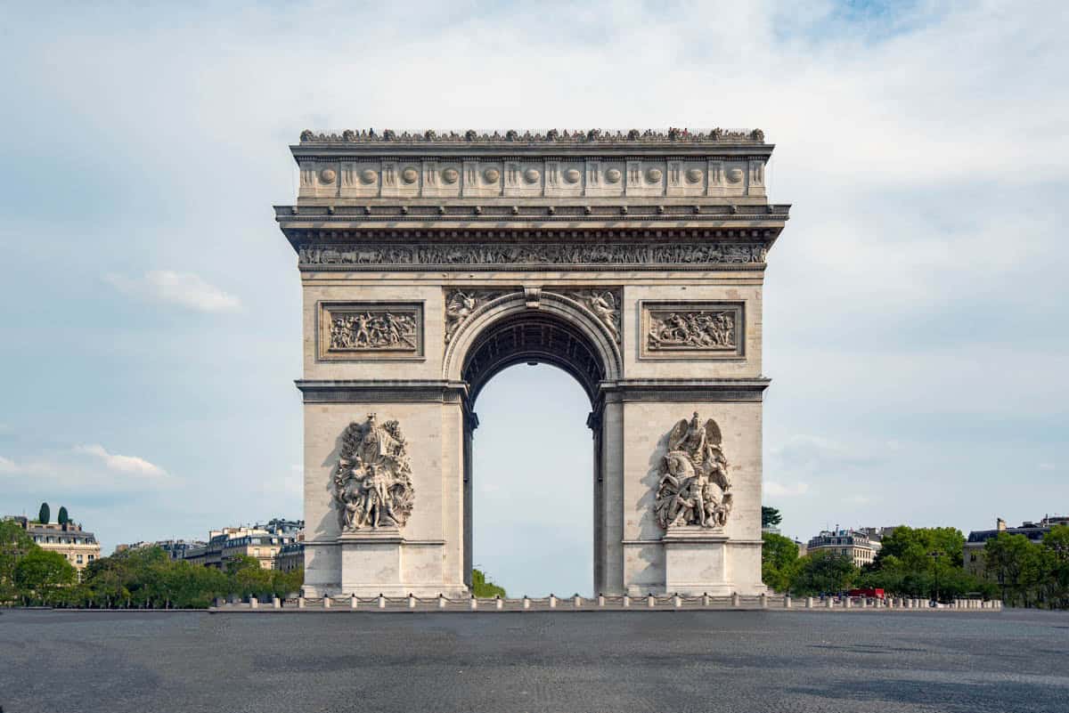 Arc de Triomphe standing beyond an open paved foreground — Arc de Triomphe, Paris, France.