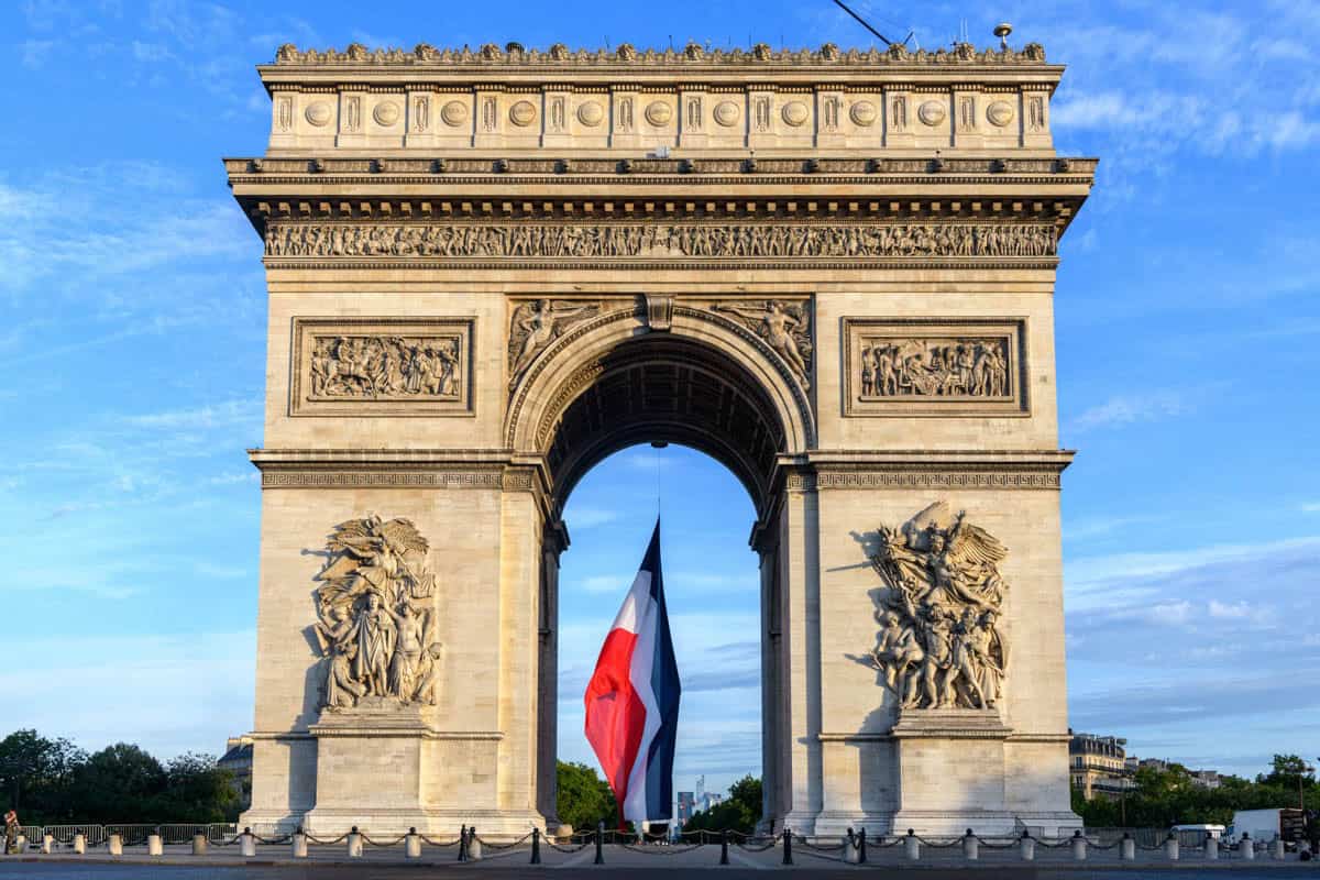 Arc de Triomphe in Paris, France pairs Arc de Triomphe front elevation with a French flag inside the arch with monument details.