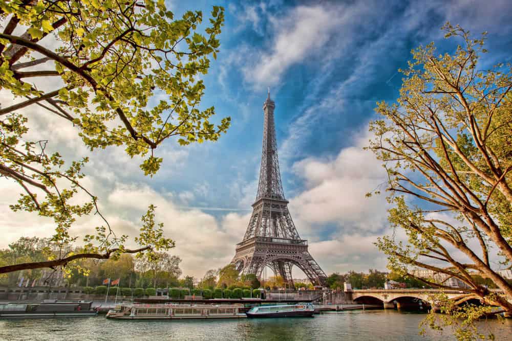 Eiffel Tower and Seine framed by arching tree branches alongside tower details at Eiffel Tower in Paris, France.