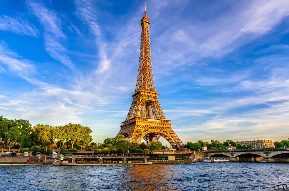 Eiffel Tower across the Seine beneath sweeping blue clouds — Eiffel Tower, Paris, France.