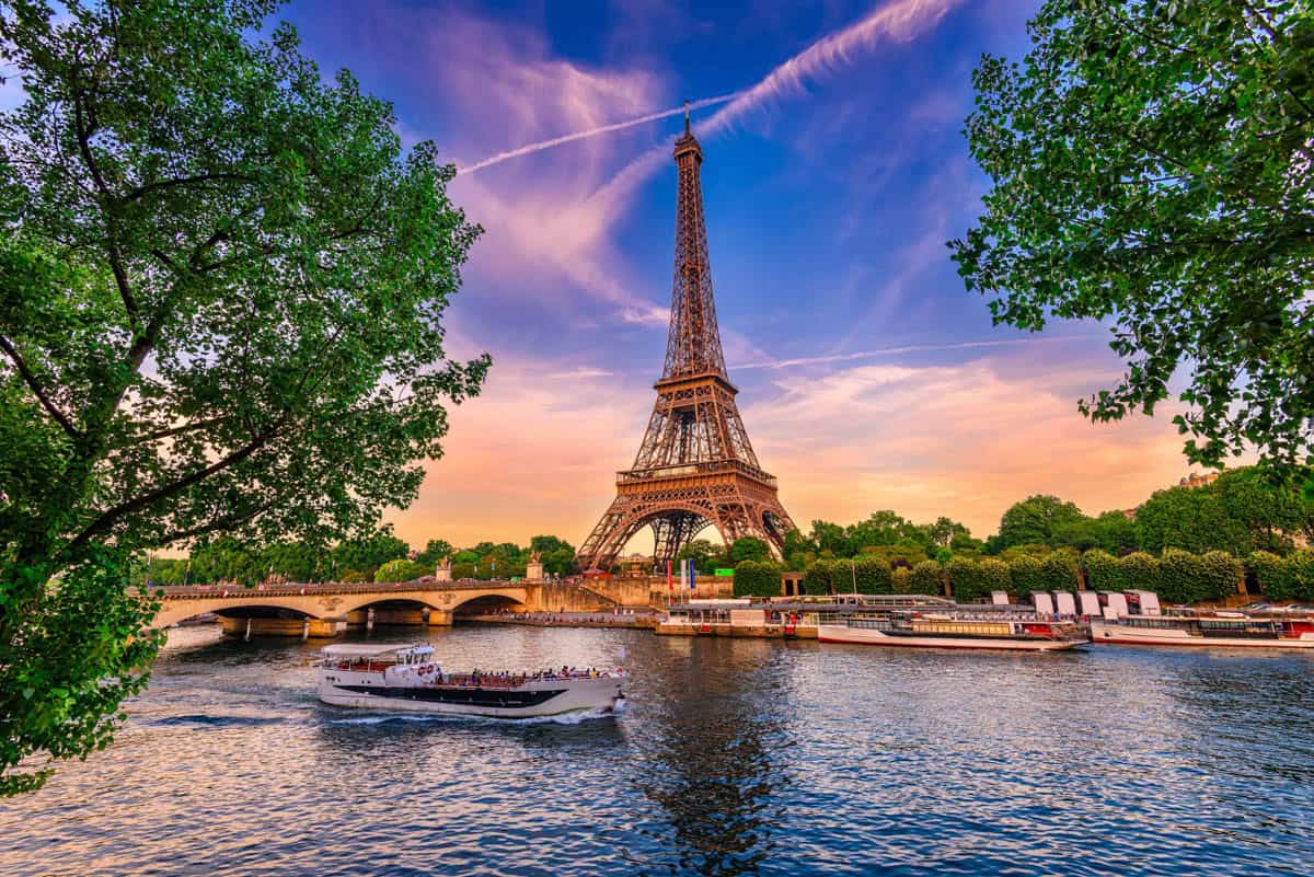 Eiffel Tower, sightseeing boat, and tree-lined Seine alongside tower details at Eiffel Tower in Paris, France.