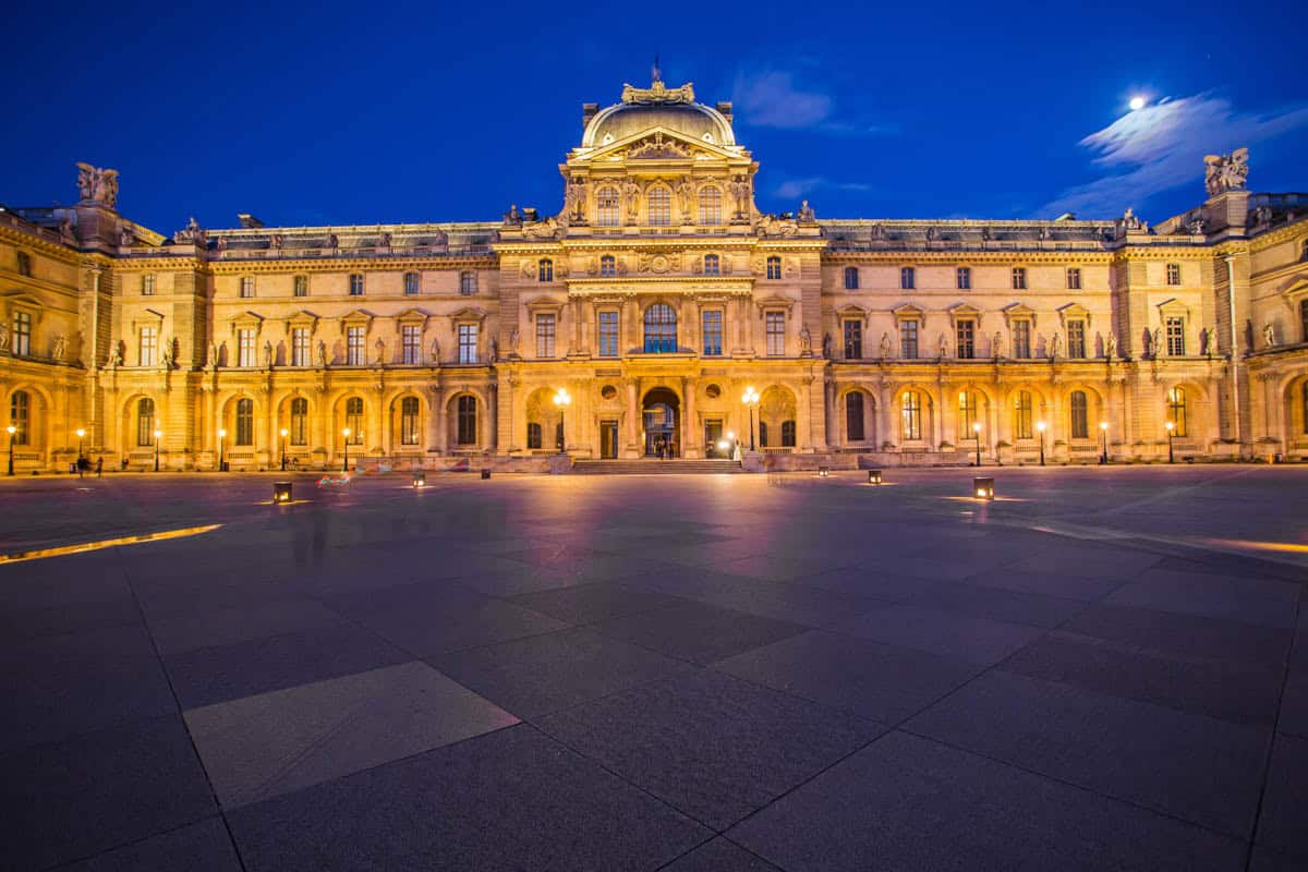 Central Louvre pavilion brightly illuminated at night framed by museum and palace architecture at Louvre Museum in Paris, France.