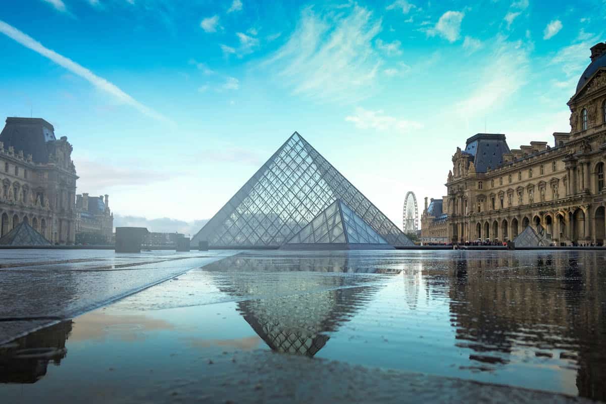 Glass Louvre Pyramid set between palace wings and reflecting pools alongside museum details at Louvre Museum in Paris, France.