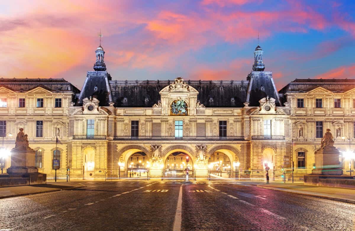 Ornate Louvre courtyard pavilion glowing beneath a sunset sky framed by museum and palace architecture at Louvre Museum in Paris, France.