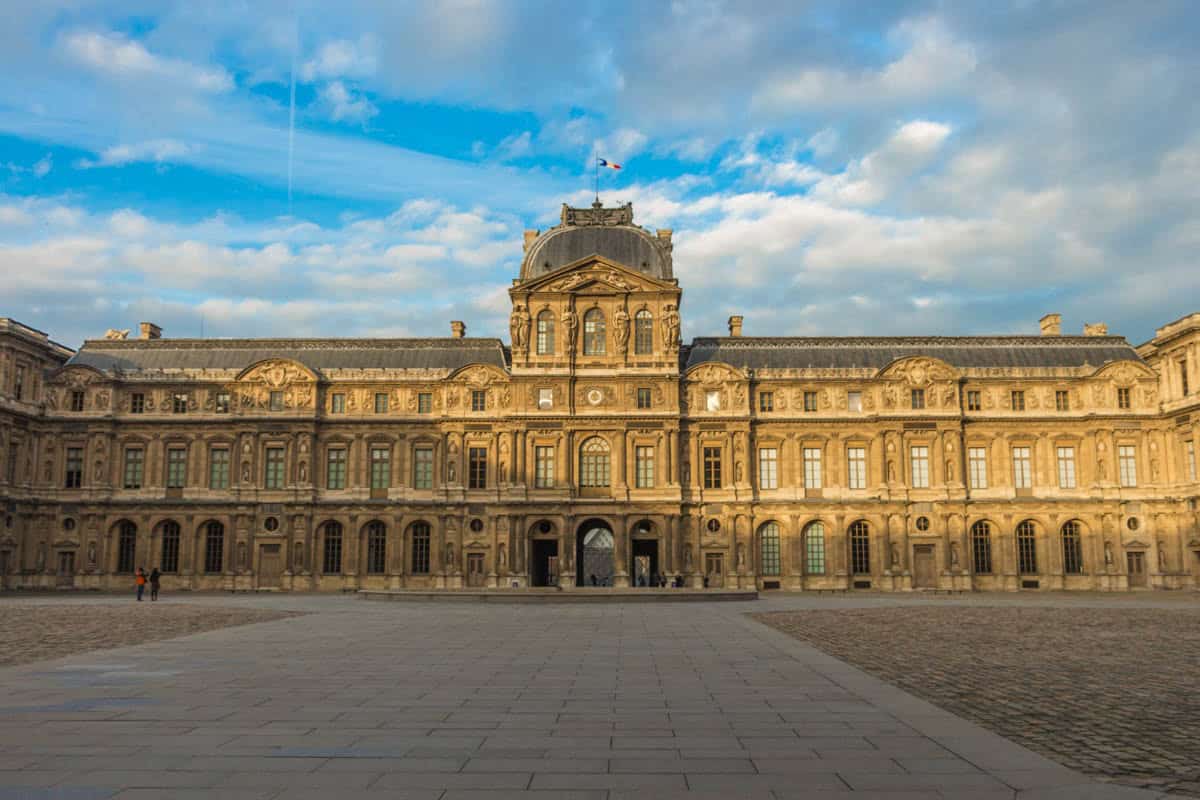 Symmetrical Cour Carrée façades around an empty paved courtyard framed by museum and palace architecture at Louvre Museum in Paris, France.