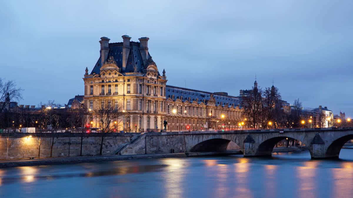 Louvre riverfront buildings and bridge reflected in the Seine at dusk — Louvre Museum, Paris, France.