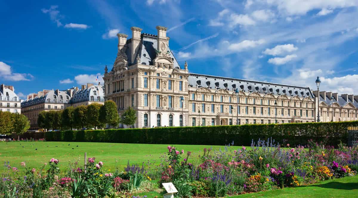 Louvre Museum in Paris, France, with Louvre wing behind green lawn and flowerbeds in the Tuileries.