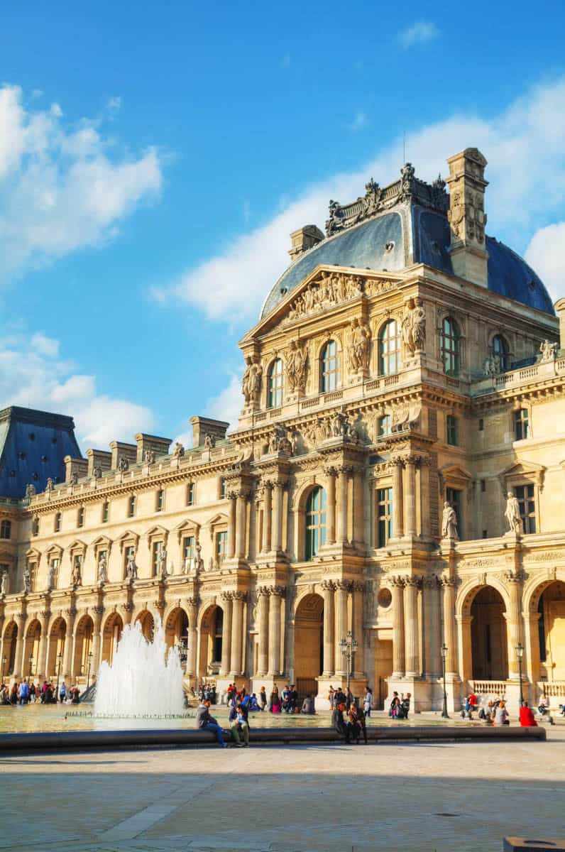 Tall palace pavilion and arcaded Louvre wing beneath a clear sky framed by museum and palace architecture at Louvre Museum in Paris, France.