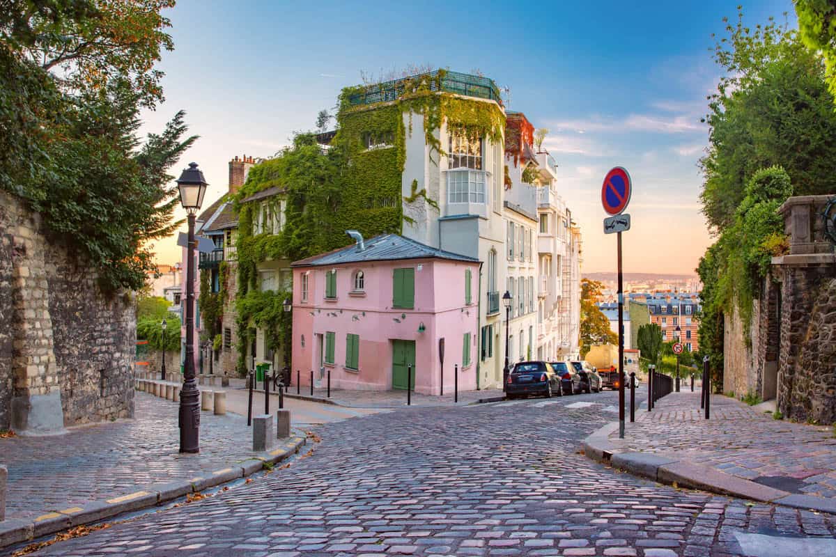 Sloping cobbled street with pastel buildings and leafy trees — Montmartre, Paris, France.