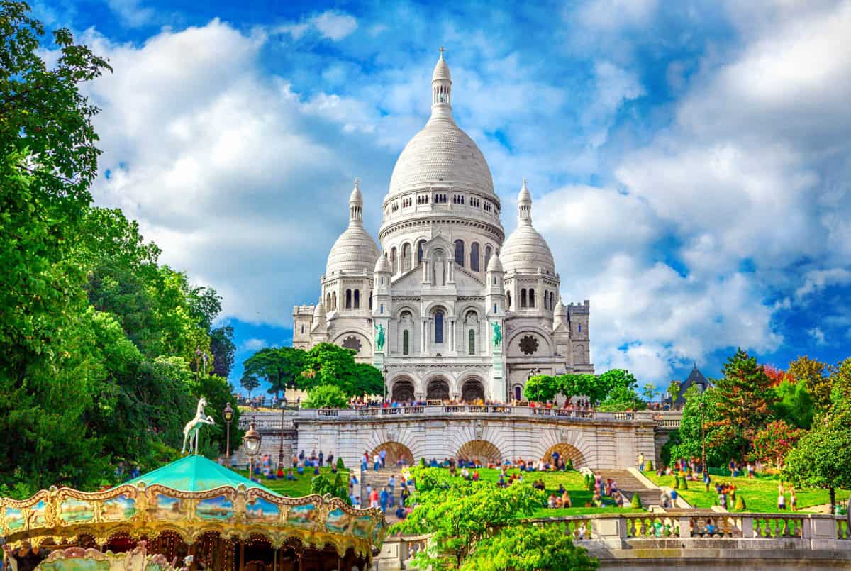 Sacré-Cœur Basilica rising above green trees and a carousel — Sacré-Cœur Basilica, Paris, France.