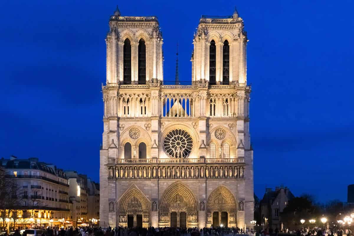 Notre-Dame west façade brightly illuminated at night framed by cathedral and gothic architecture at Notre-Dame Cathedral in Paris, France.