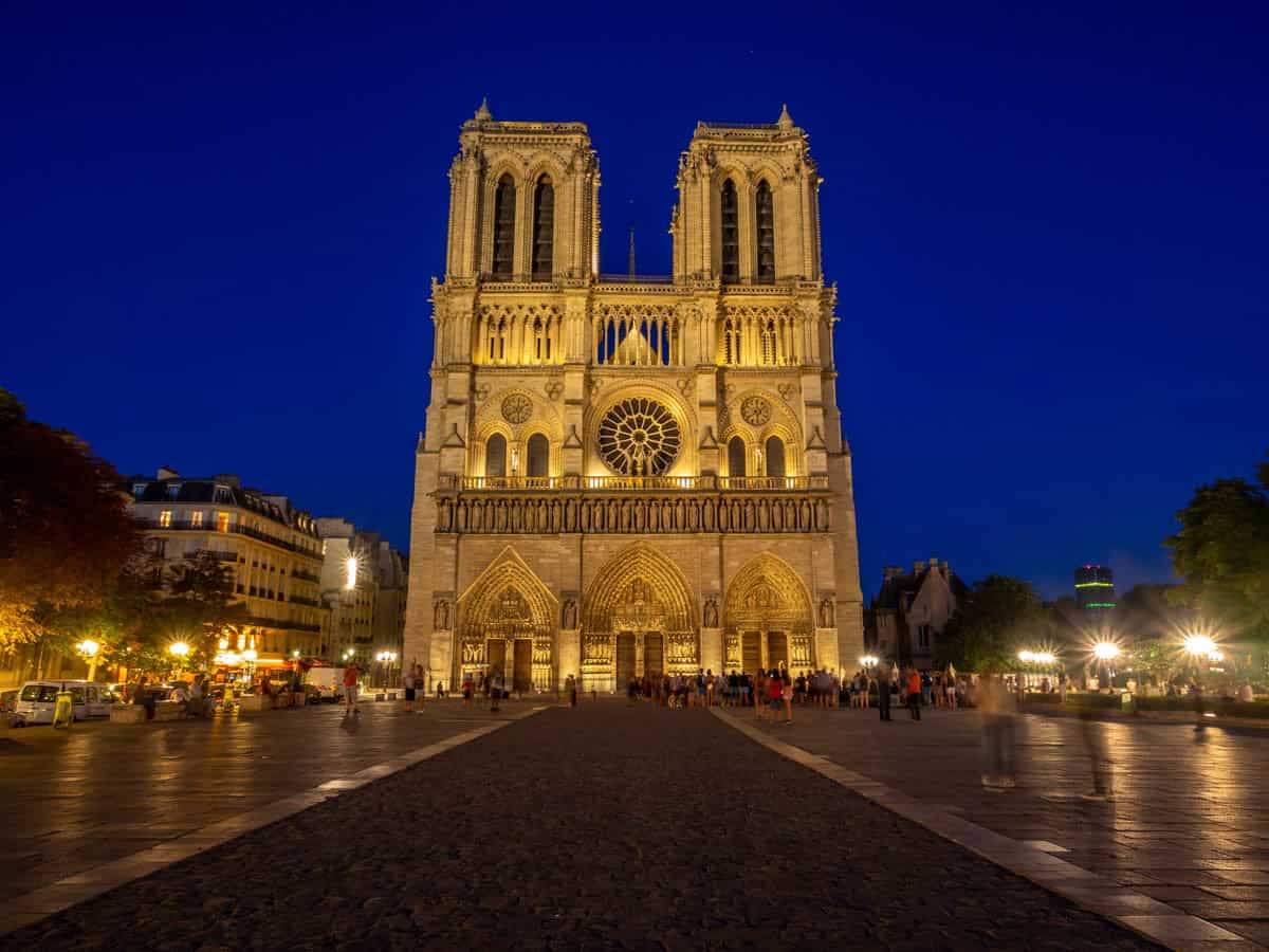 Notre-Dame west towers glowing above the evening plaza alongside cathedral details at Notre-Dame Cathedral in Paris, France.
