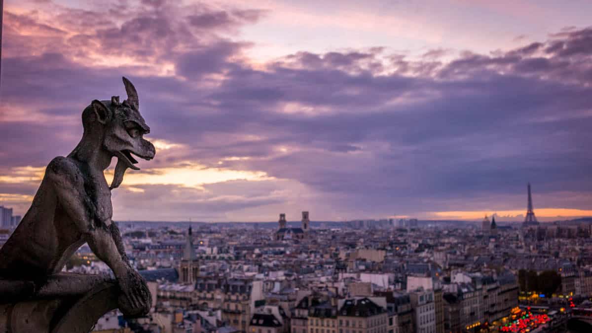 Stone gargoyle overlooking Paris rooftops and the Eiffel Tower framed by cathedral and gothic architecture at Notre-Dame Cathedral in Paris, France.