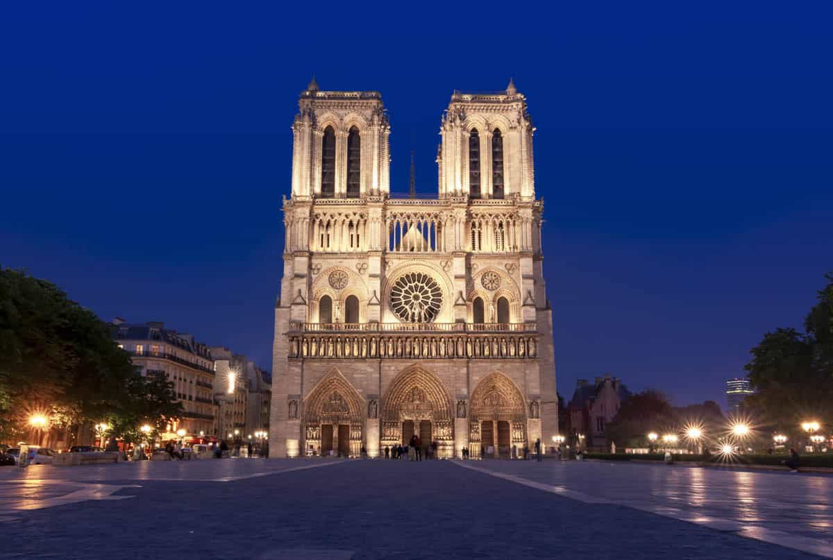 Notre-Dame west façade illuminated across the dark plaza alongside cathedral details at Notre-Dame Cathedral in Paris, France.