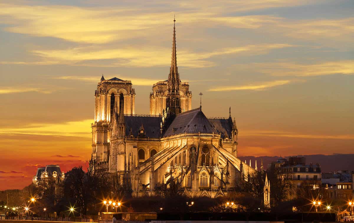 Notre-Dame Cathedral in Paris, France, with Notre-Dame apse and spire glowing beside the Seine at sunset.