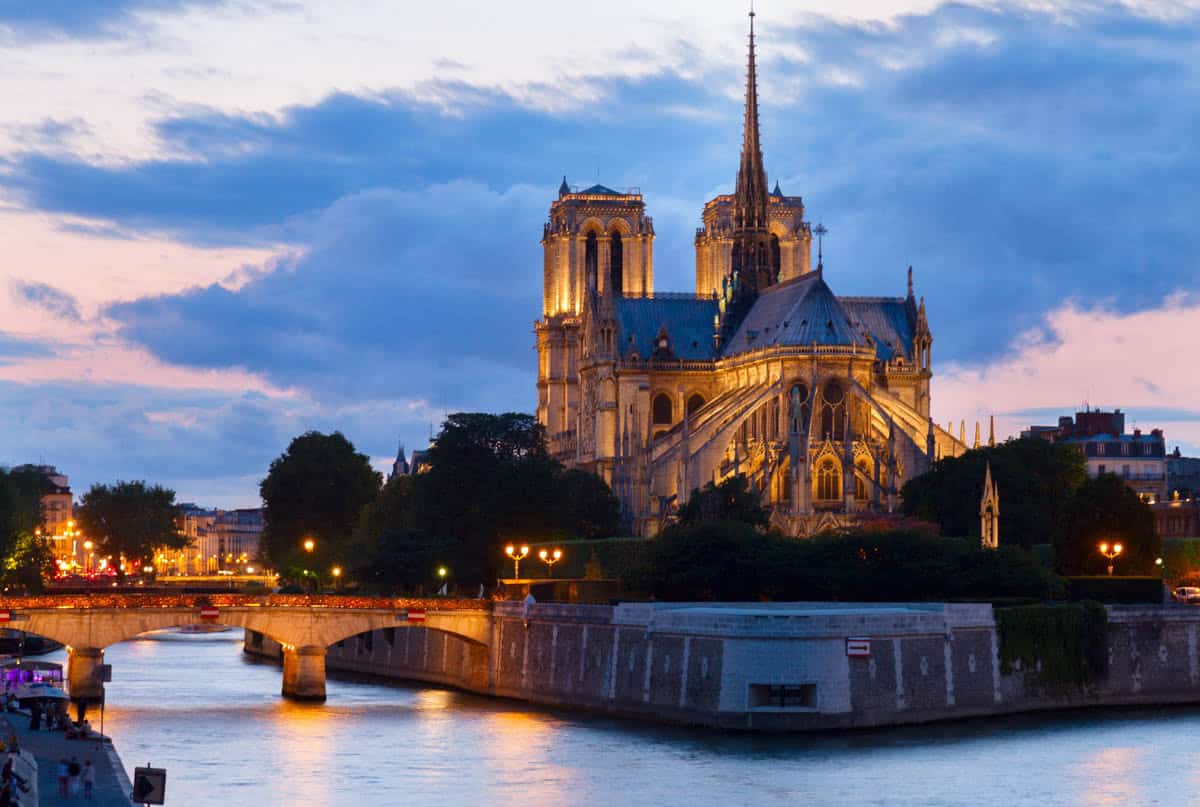 Notre-Dame Cathedral in Paris, France, featuring Notre-Dame west façade illuminated against a dark blue sky beside cathedral features.