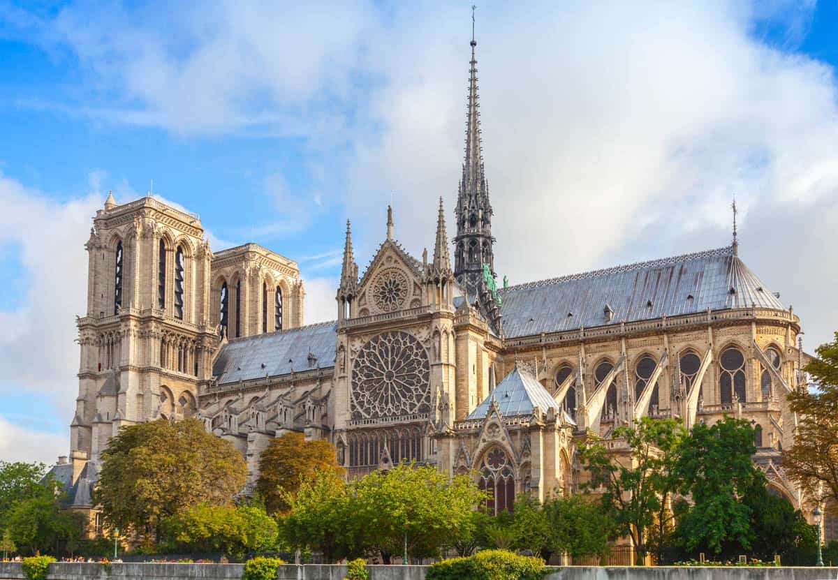 Notre-Dame apse, spire, and flying buttresses behind leafy trees alongside cathedral details at Notre-Dame Cathedral in Paris, France.