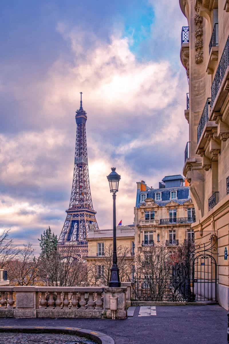 Eiffel Tower framed between an ornate stone building and riverside architecture framed by tower and Paris monument at Eiffel Tower in Paris, France.
