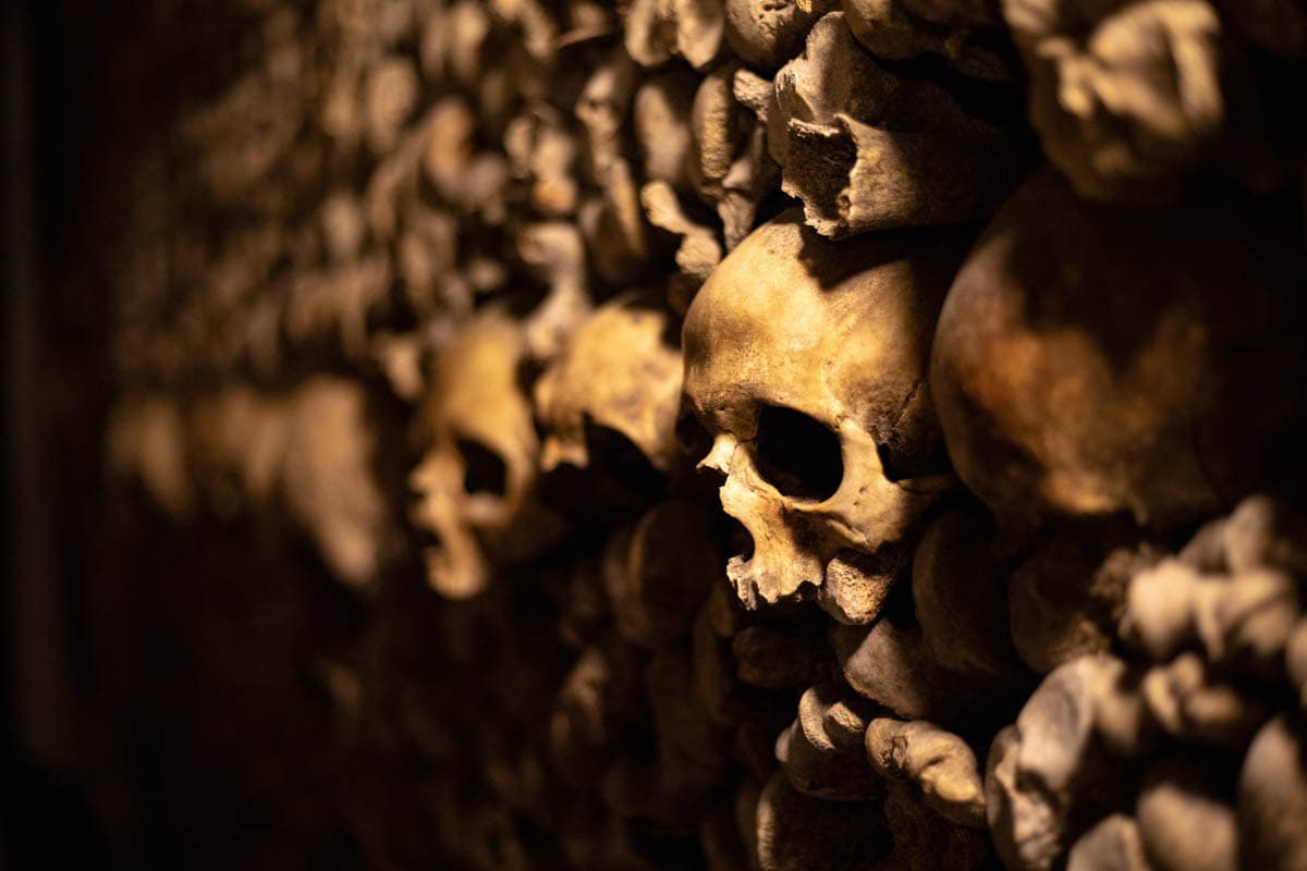 Paris Catacombs in Paris, France, with skulls embedded among warm-lit stacks of human bones.