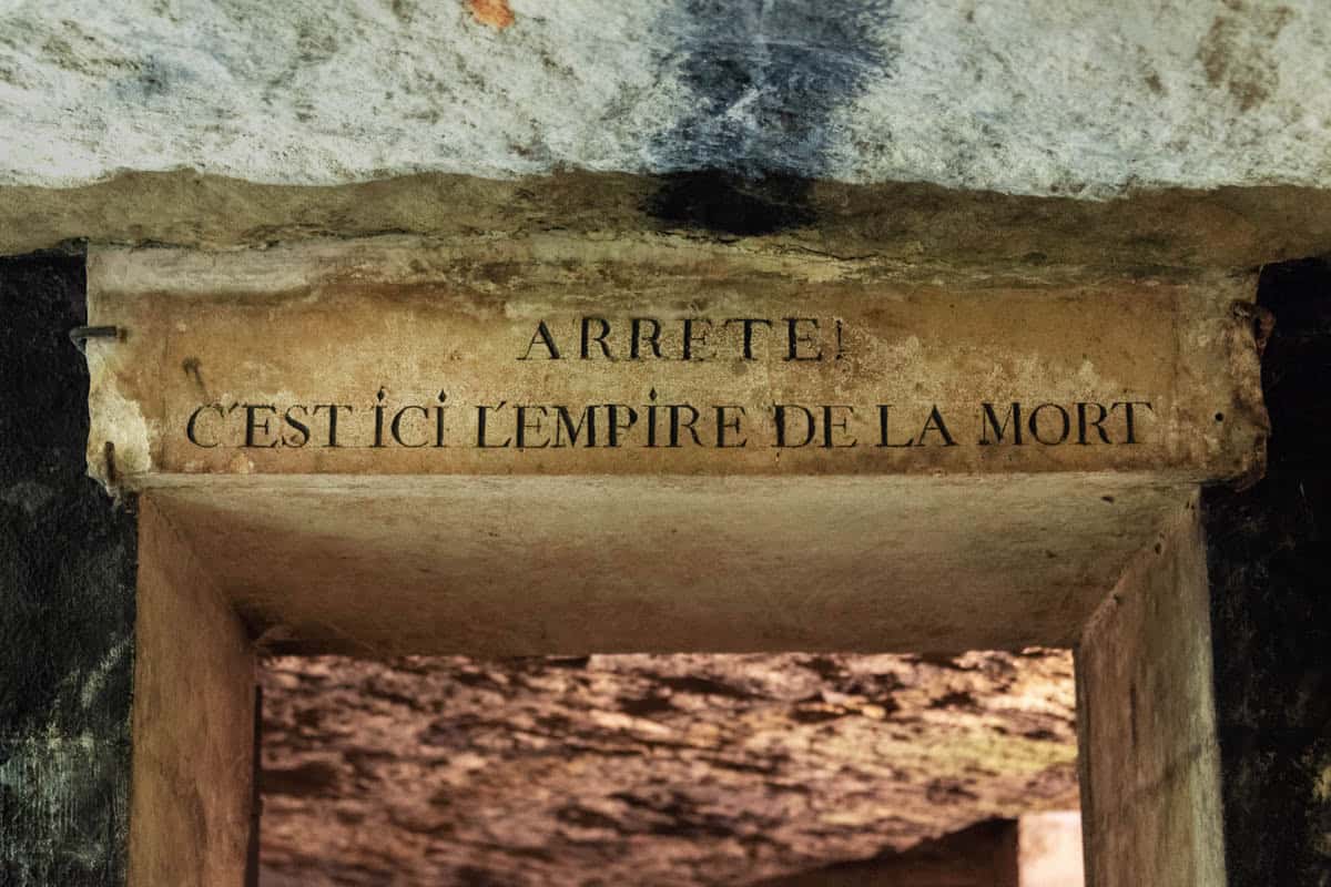 Paris Catacombs in Paris, France, with historic French warning inscription carved above a low stone passage.