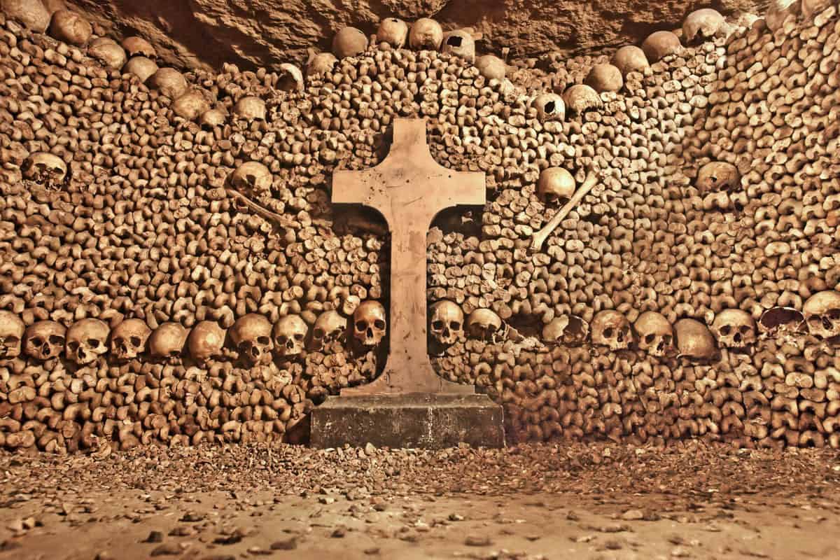 Paris Catacombs in Paris, France, with stone cross surrounded by symmetrical rows of skulls and bones.