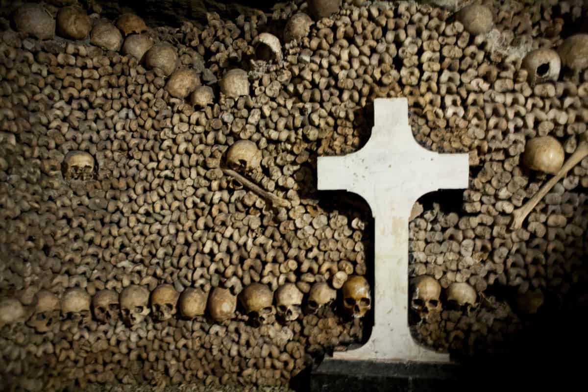 White stone cross set against carefully stacked skulls and bones at Paris Catacombs in Paris, France.