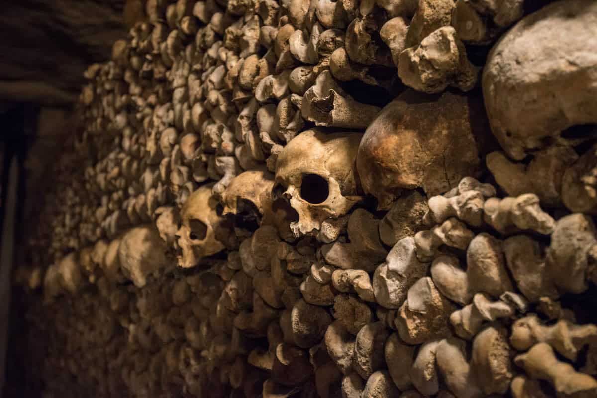 Paris Catacombs in Paris, France, with irregular cluster of skulls and bones in a dim ossuary wall.
