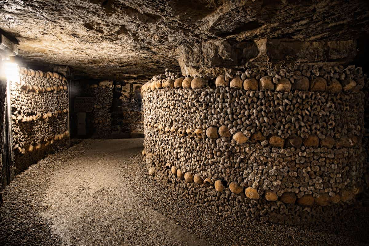 Paris Catacombs in Paris, France, with curving gallery with skull-and-bone walls leading into darkness.