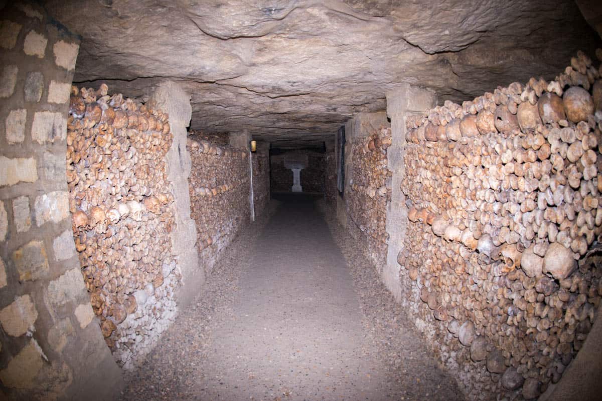 Paris Catacombs in Paris, France, with long underground corridor bordered by stacked bones on both sides.