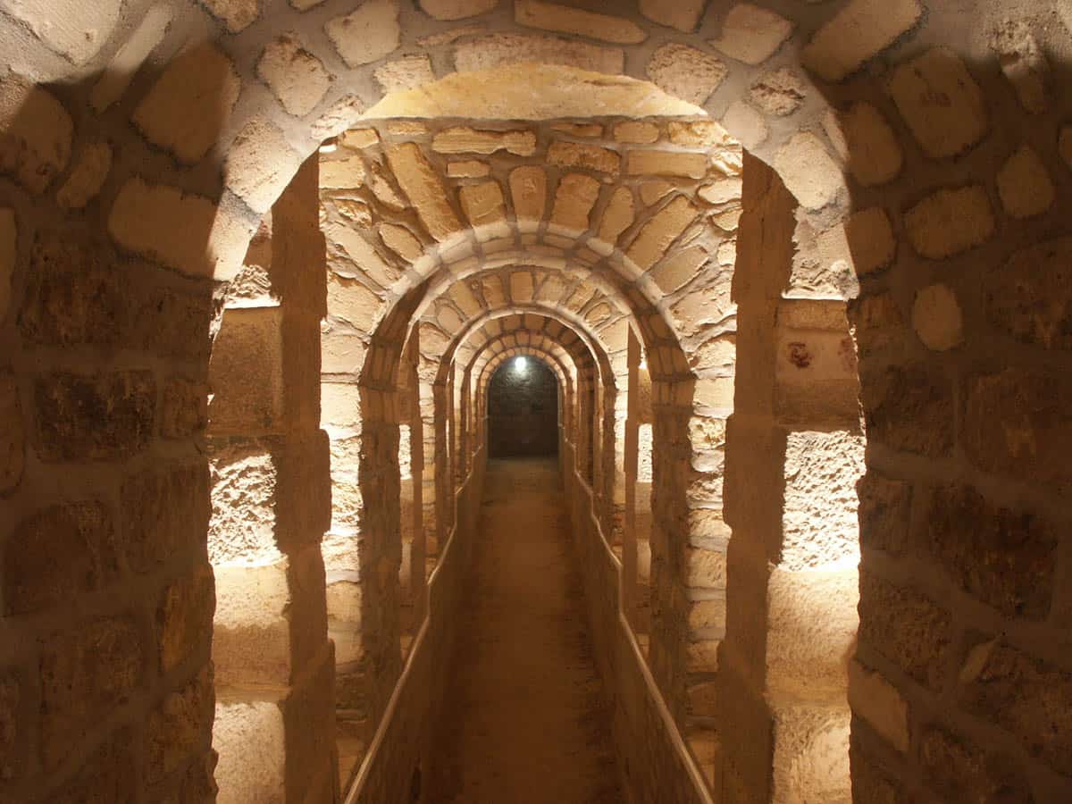 Paris Catacombs in Paris, France, with stone-vaulted underground gallery with repeating arches and warm lights.