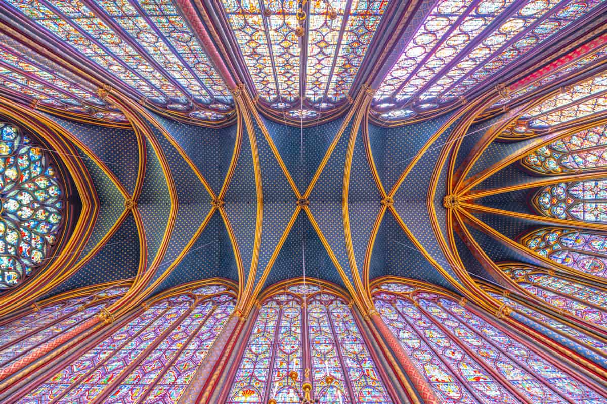 Sainte-Chapelle in Paris, France, featuring radiating ceiling ribs crossing star-patterned vault panels beside stained glass features.