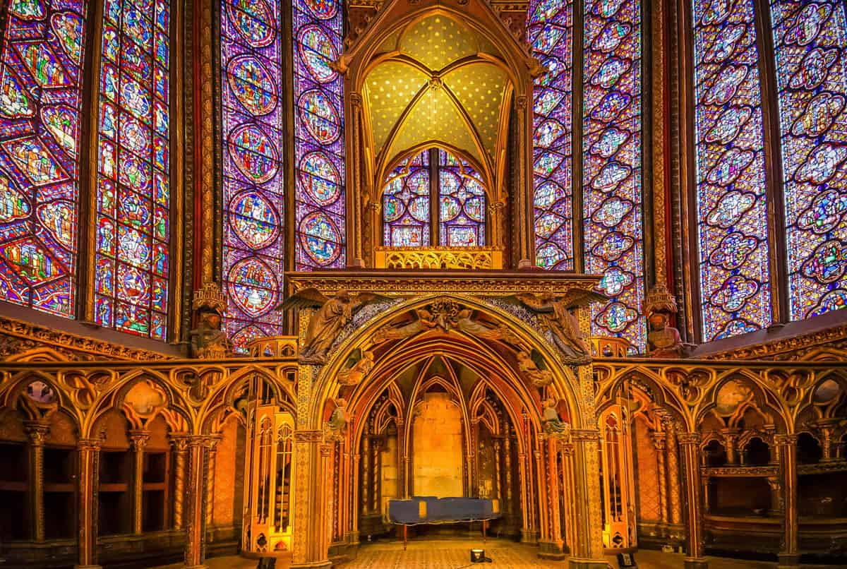 Gilded arcade and stained-glass walls glowing above the altar framed by stained glass and gothic chapel at Sainte-Chapelle in Paris, France.