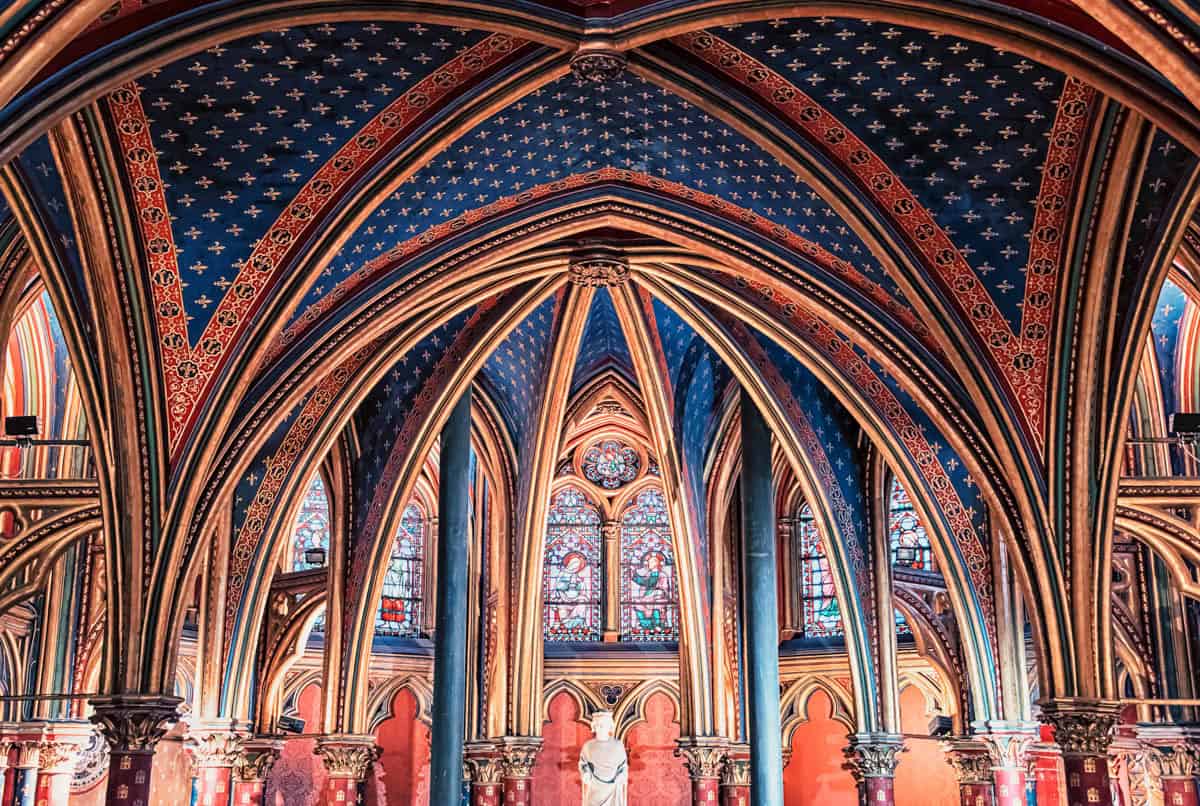 Lower chapel with colorful columns, painted arches, and seated visitors with gothic chapel details around Sainte-Chapelle in Paris, France.