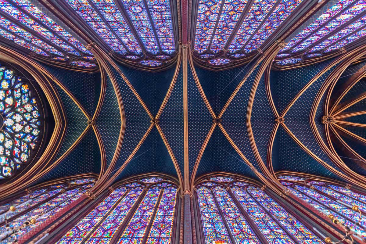 Apse area enclosed by tall stained-glass windows and painted vaults with gothic chapel details around Sainte-Chapelle in Paris, France.