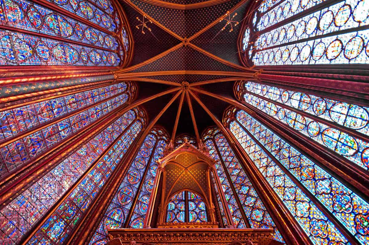 Sainte-Chapelle in Paris, France, featuring rising pattern of stained glass, clustered ribs, and starry ceiling panels beside stained glass features.