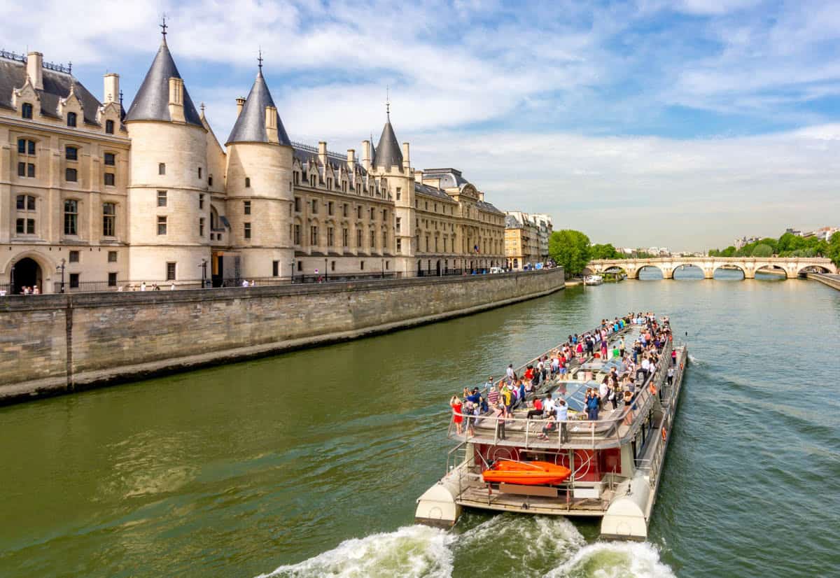 Seine River in Paris, France pairs open-deck sightseeing boat beside the Conciergerie riverfront with river details.