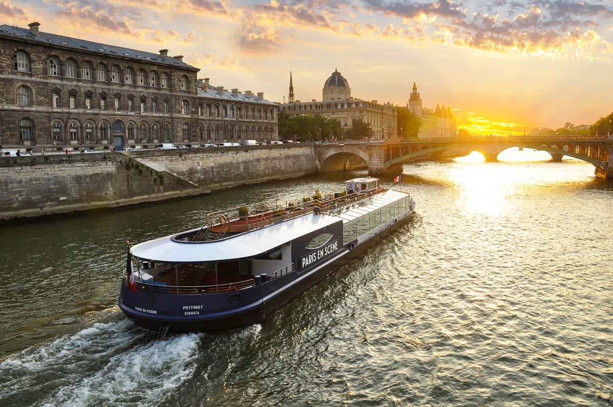 Seine River in Paris, France, with low passenger boat moving along the Seine beneath a glowing sky.