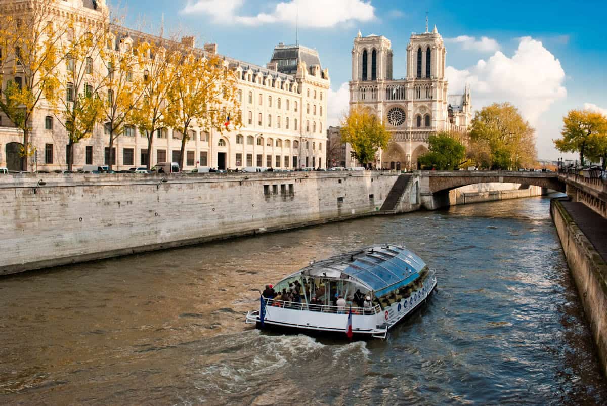 Sightseeing boat traveling past the Île de la Cité riverfront and cathedral set among river elements at Seine River in Paris, France.
