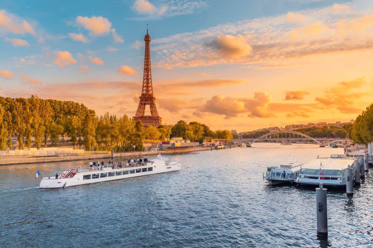 Seine River in Paris, France pairs Eiffel Tower, bridges, and moored boats in golden evening light with river details.