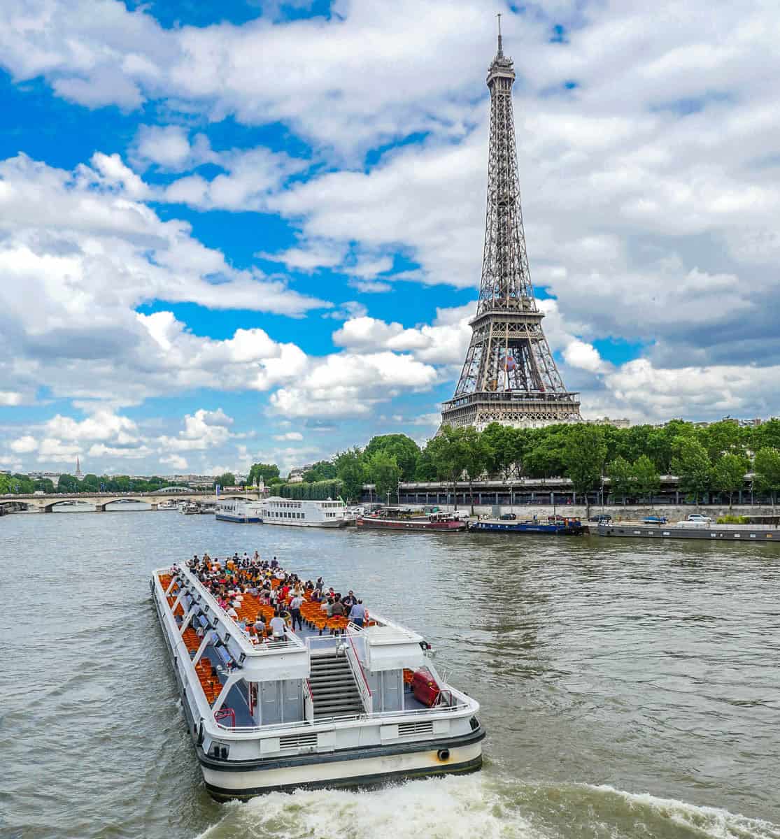Seine River in Paris, France pairs open-deck cruise boat heading toward the Eiffel Tower with river details.