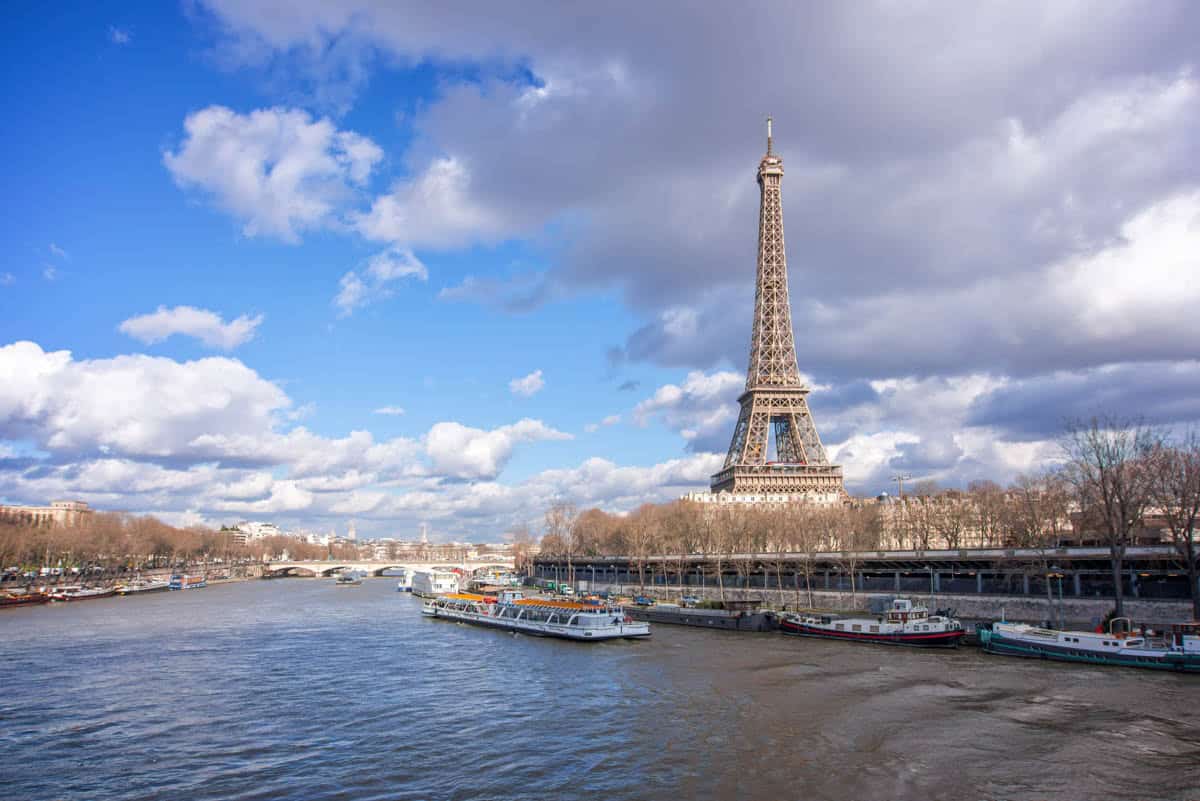 Seine River in Paris, France pairs Eiffel Tower and excursion boat under a cloud-filled sky with river details.