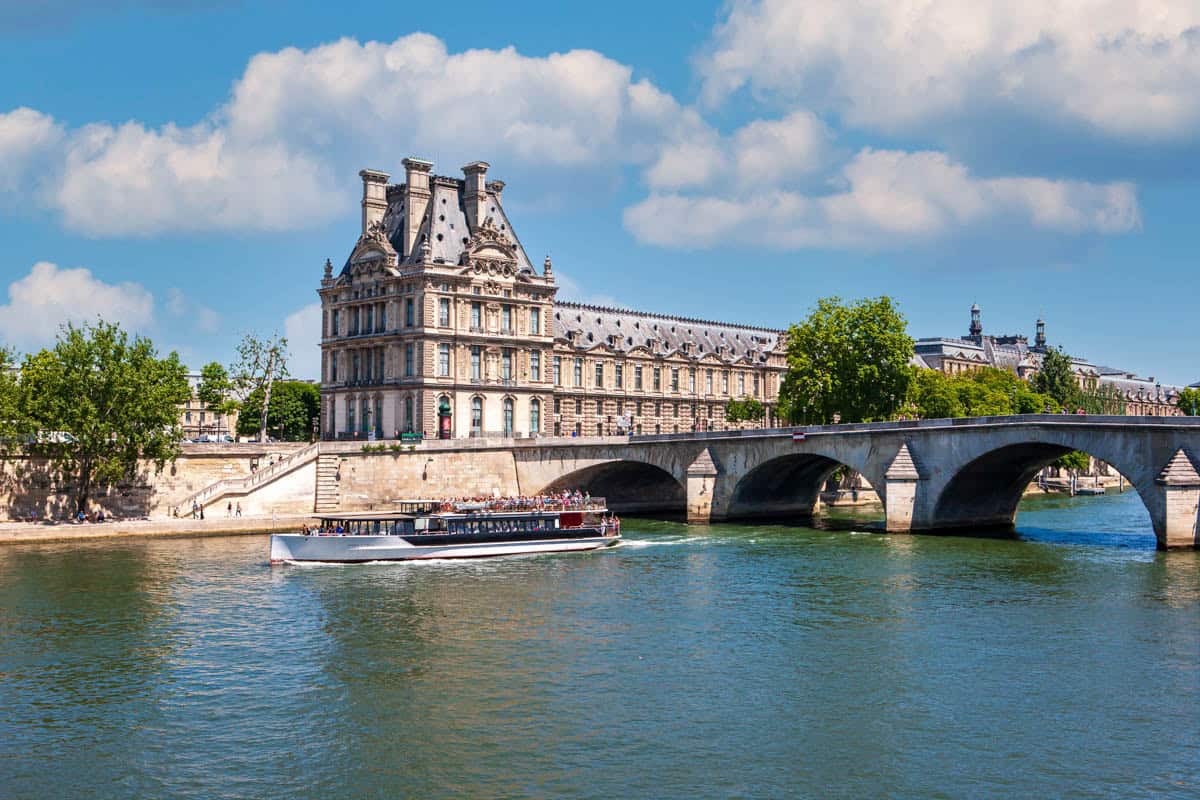Seine River in Paris, France pairs Conciergerie buildings, stone bridge, and cruise boat on the Seine with river details.