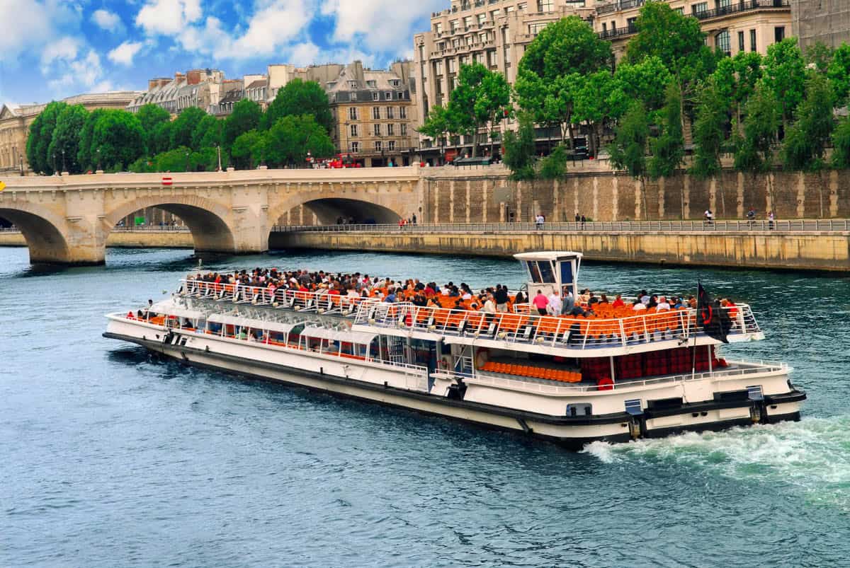 Seine River in Paris, France, featuring large glass-roof sightseeing boat passing a stone bridge beside river features.