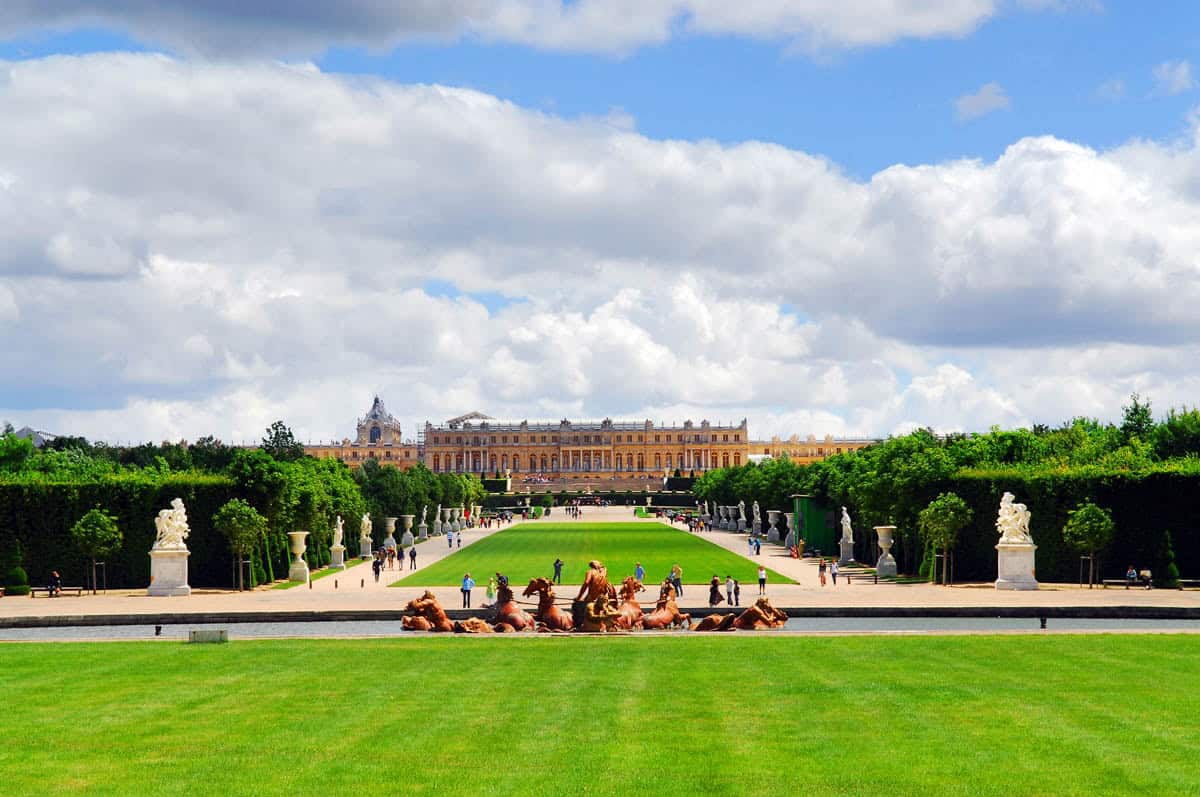 Palace buildings beyond an expansive lawn and tree-lined garden framed by palace and formal gardens at Palace of Versailles in Versailles, France.