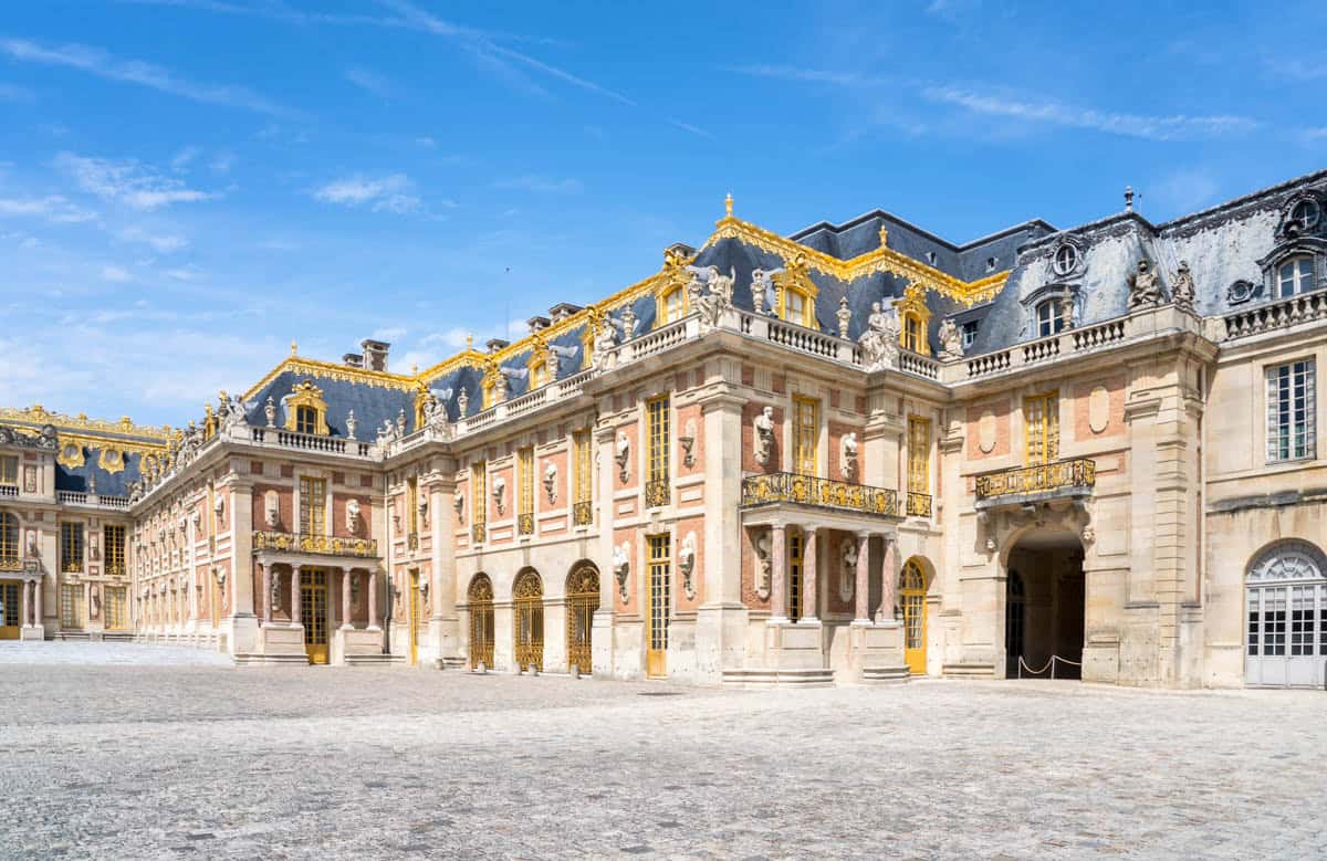 Stone-and-gilt palace wings enclosing an open courtyard — Palace of Versailles, Versailles, France.