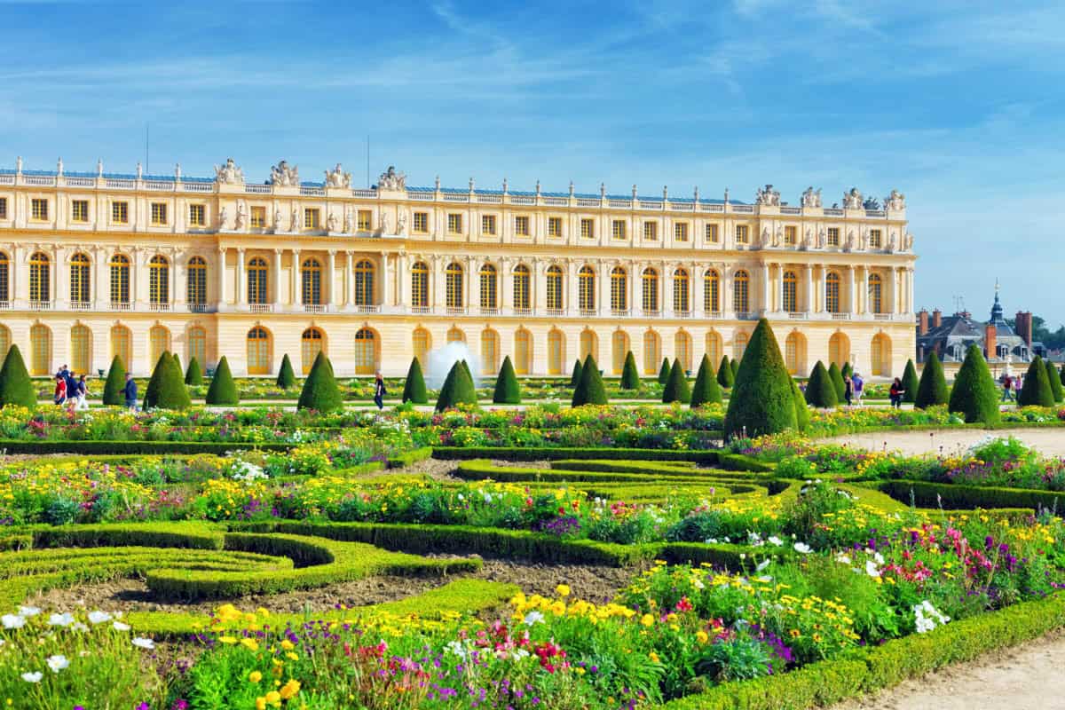 Palace façade overlooking colorful formal gardens framed by palace and formal gardens at Palace of Versailles in Versailles, France.