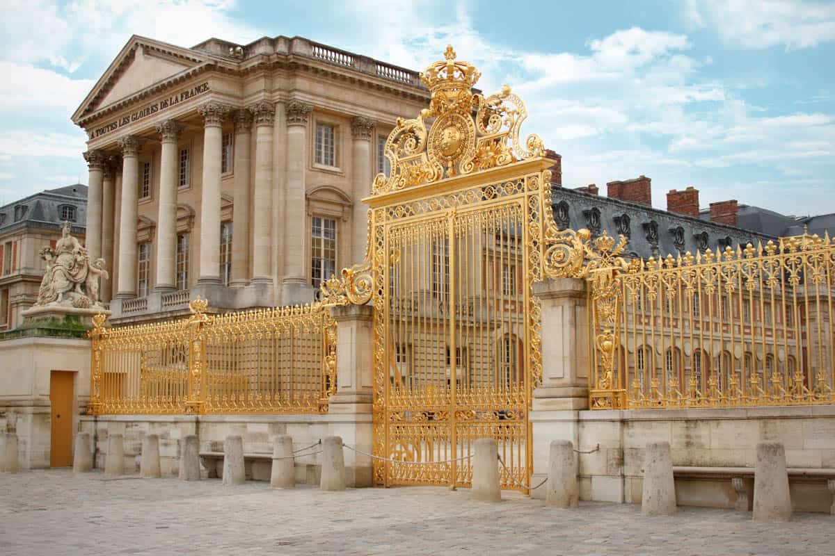 Gilded reclining figures and fountain basin among clipped hedges framed by palace and formal gardens at Palace of Versailles in Versailles, France.