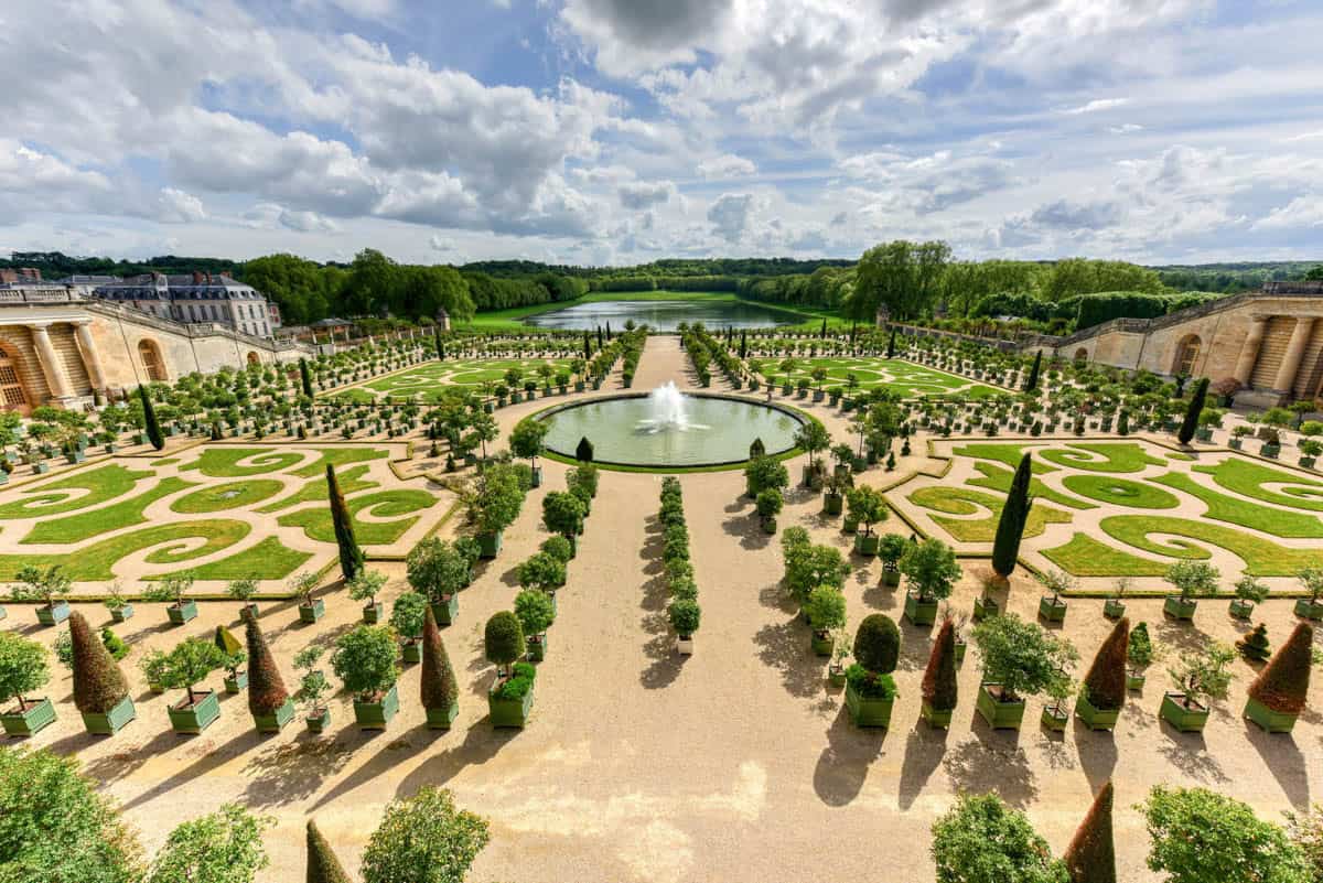 Formal parterres and long reflecting pools seen from above framed by palace and formal gardens at Palace of Versailles in Versailles, France.
