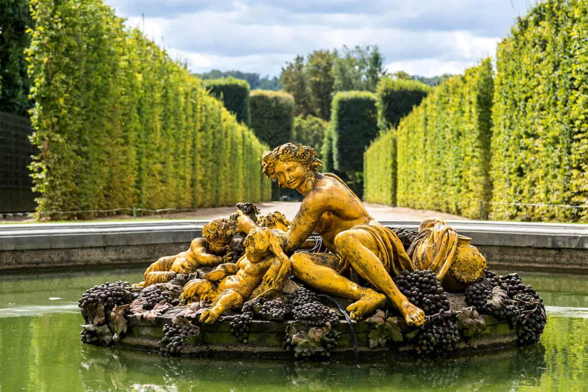 Symmetrical lawn and flowerbeds leading to a garden pavilion framed by palace and formal gardens at Palace of Versailles in Versailles, France.